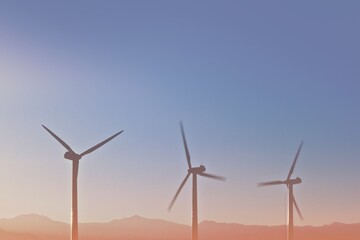 Obraz premium Three wind turbines against a clear sky and distant mountains.