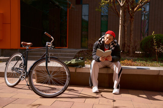 Handsome young man enjoying a sunny day reading by his bicycle in the city
