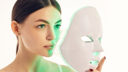 Close up woman holding green LED mask for facial skincare therapy. Concept of beauty device advertising, selfcare routine, antiaging care, skin tone and cosmetic treatment. © master1305