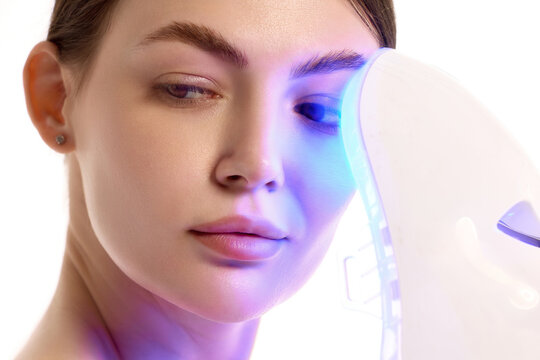 Close up woman using blue LED mask for facial skincare therapy. Concept of beauty device advertising, selfcare routine, acne care, antiaging and skin treatment.