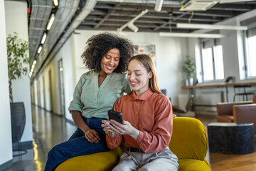 Fototapeta premium Diverse businesswomen collaborating using smart phone in modern office