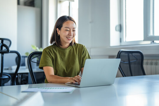 Young asian woman smiling while working on laptop