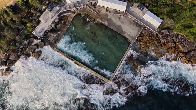 Aerial view of the historic Coogee Beach ocean pool with crashing waves against the rocky coastline in Sydney, New South Wales, Australia.