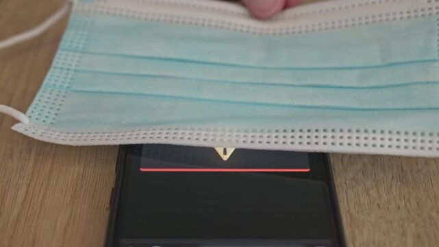 Generic mobile interface showing a pandemic warning and mandatory mask alert with a real protective mask in the frame.