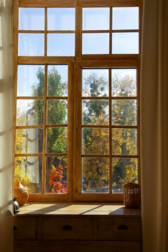 View of colorful trees through a wooden window on a bright day in autumn with sunlight shining in the room