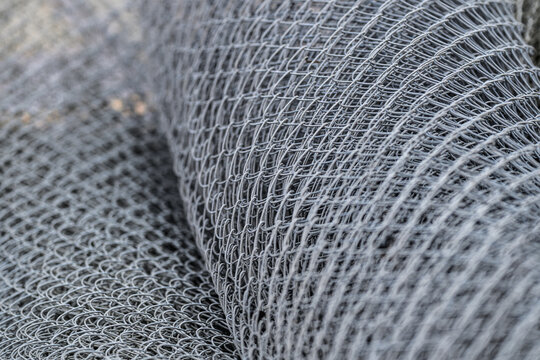 Stacked grey chain link fence rolls creating abstract industrial texture.