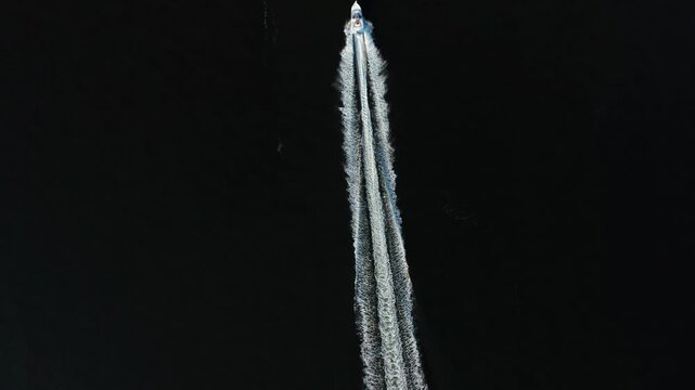 Small powerboat races forward leaving twin white foam trails that form a straight line across the dark river.