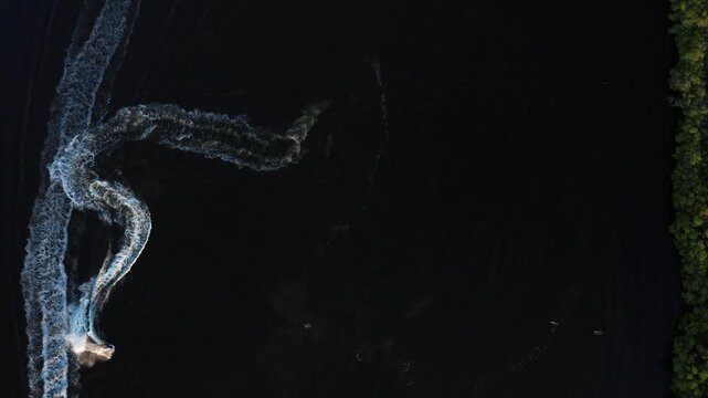 Small motorboat races along the dark Braden River, leaving bright S-shaped wakes beside a wall of green mangroves.