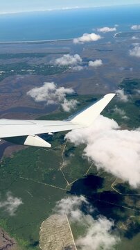 Scenic aerial view from a passenger airplane window overlooking the wing, white clouds, and the landscape below during daylight. Ideal for travel, aviation, commercial airline, transportation, vacatio