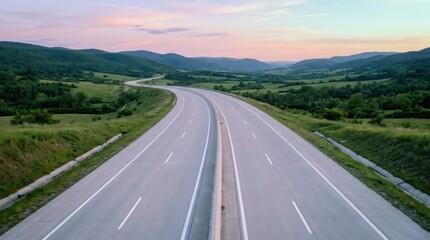 Obraz premium Empty multi-lane highway stretching through summer mountain landscape. Scenic asphalt road winding into distance at sunset. Infrastructure journey concept. Outdoor travel background.