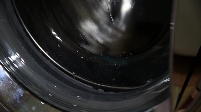 Washing machine drum in motion with laundry items including mesh bag and patterned fabric, clean cycle process of clothes, household appliance action indoors, modern home cleaning technology
