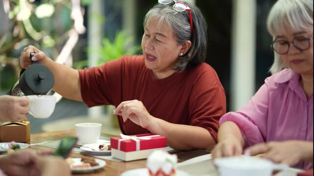 Senior friends serve drinks, share food and enjoy warm conversations around the table. Caring friendship, generosity, active aging and joyful dining create memorable social moments together.