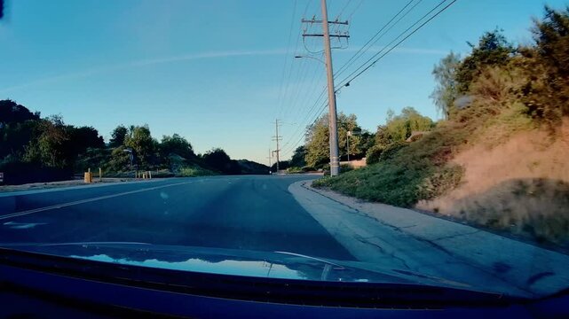A dashcam view of Mulholland Hwy. winding through hilly landscape under clear blue sky, power poles and lines lining roadside, scenic drive through natural terrain of California.