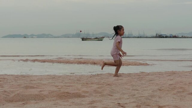 slow motion of happy preschool child girl running on the sea beach in Pattaya, Thailand