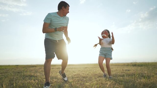 Father and daughter playing ball. Family enjoying sport together outdoors. Girl throws ball to father. Family bonding through sport. lifestyle family playing ball. Father daughter laugh enjoying sport