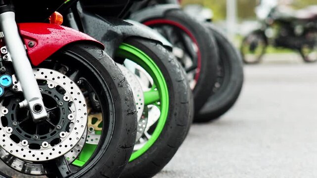Front wheels of multiple motorcycles parked in a line, showing red fender, disc brakes, and wet surfaces from rain, suggesting recent weather, slow motion, copy space