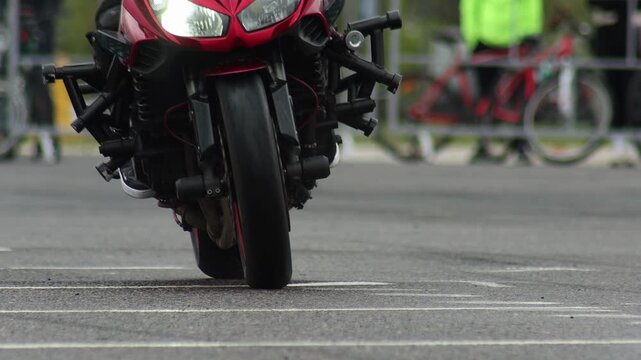 Red sports motorcycle performing impressive wheelie stunt during outdoor event, showcasing vehicle agility and rider skill on asphalt surface, front wheel off ground, slow motion, copy space