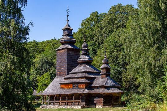 Ancient Ukrainian wooden church in green forest landscape. Traditional rustic orthodox wooden church with shingle roofs in rural heritage museum. Historic architecture landmark