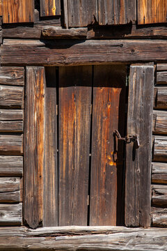 Vintage wooden door on old log cabin wall with rusty chain. Old rustic barn door with unique wood texture and locked chain on authentic weathered log house backdrop
