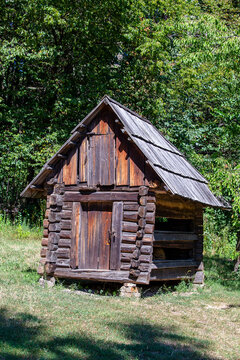 Small vintage wooden log cabin barn in countryside landscape. Rustic wooden storehouse with shingle roof on green grass field. Historical countryside structure for ethnic heritage tourism