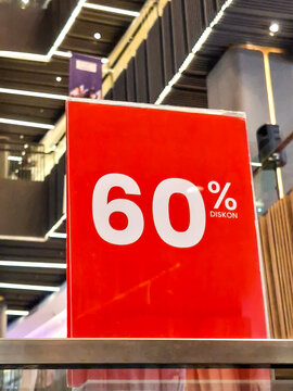 close-up shot of a bright red promotional sign displaying a "60% DISKON" announcement inside a shopping mall, with blurred store lights in the background.