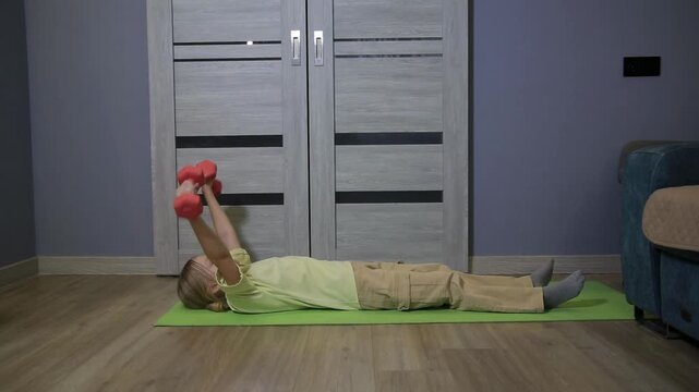 Young girl performing dumbbell exercises on yoga mat at home, engaging in fitness routine for upper body strength and physical well-being indoors.