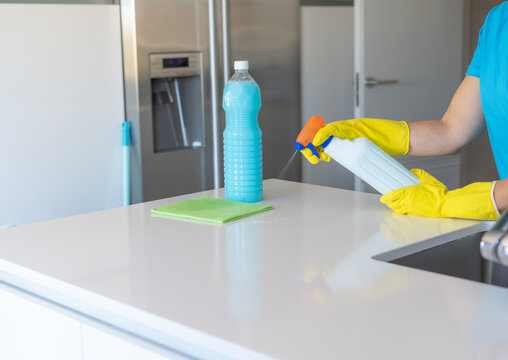 Person cleaning kitchen counter with spray detergent and gloves