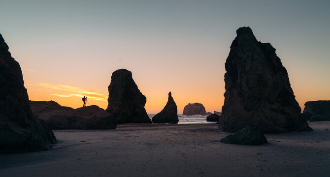 Oregon coast at sunset with photographer standing on rock capturing the stunning view of sea stacks in Bandon, Oregon, PNW, USA