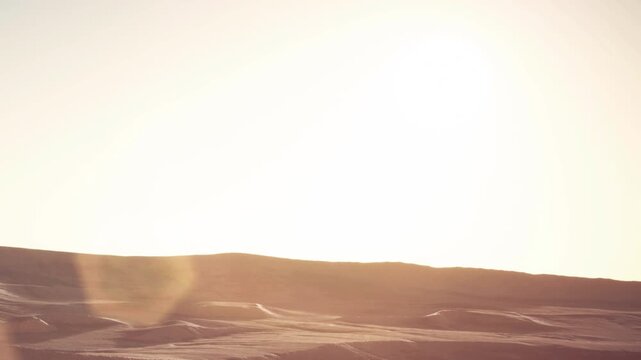 A bright sun rises over the sandy dunes in a desert. The warm light shines on the smooth contours of the dunes. The scene captures the beauty of nature in the early morning.