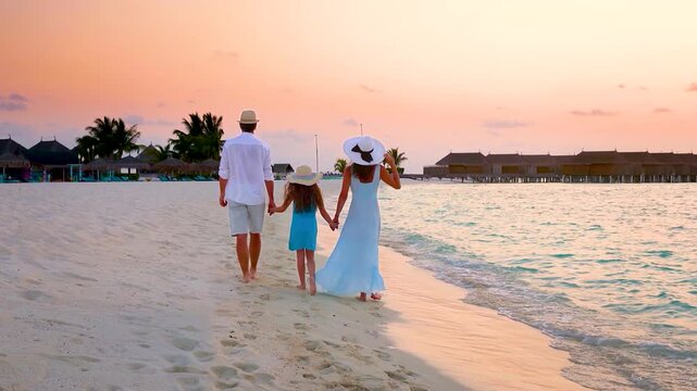 A elegant family walks on a tropical paradise beach in the luxurious Maldives islands during sunset time