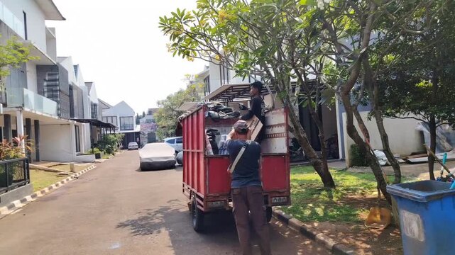 Two sanitation workers are seen discarding and sorting waste for recycling on a three-wheeled vehicle.