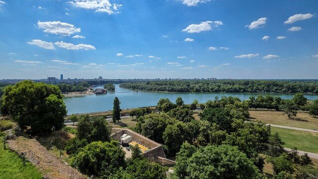 View of the Sava and Danube river confluence from the historic Belgrade Fortress, with lush trees and parkland under a blue sky in Beograd, Grad Beograd, Serbia.