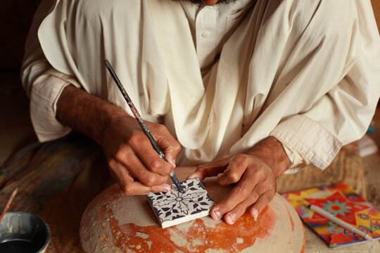 View of a craftsman painting a traditional floral pattern on a ceramic tile in Hala, Sindh, Pakistan.