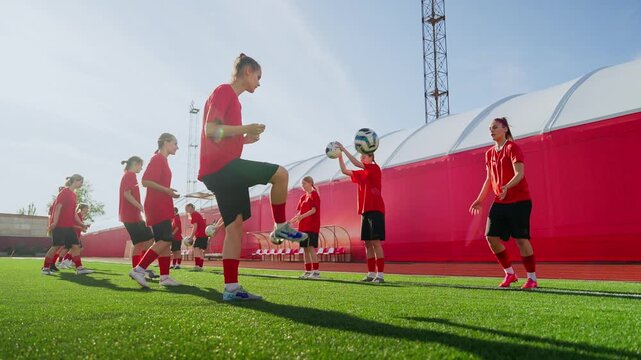 Womens soccer team training together on sunny artificial turf field, practicing passing drills, ball control and coordination in red training kits
