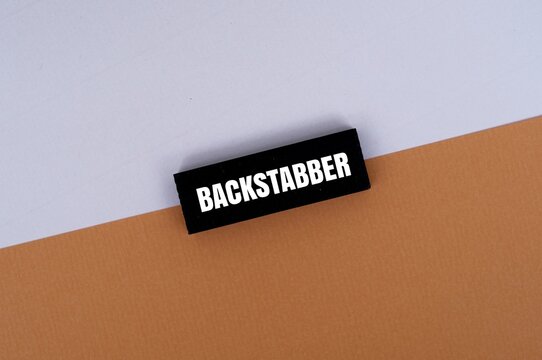 A coloured block with "BACKSTABBER" text against coloured background. Concept of betrayal, toxic relationships, and dishonesty