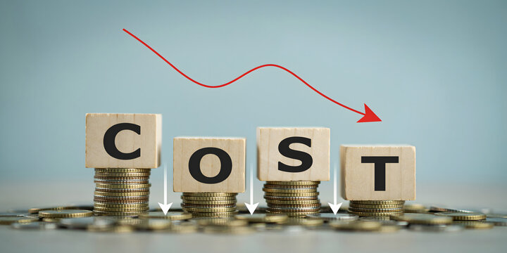 Wooden blocks spelling the word cost placed on stacks of coins with a red downward trending arrow indicating a reduction in business expenses