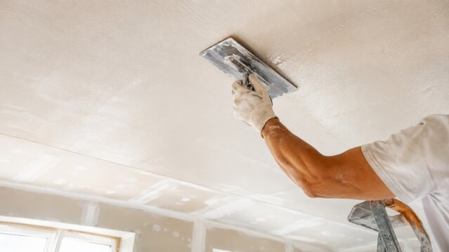 Worker applying plaster to ceiling with a trowel, renovating a room