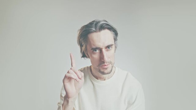 Middle-aged man raising index finger, close up portrait on neutral background in light sweater, attention and instruction gesture, communication concept