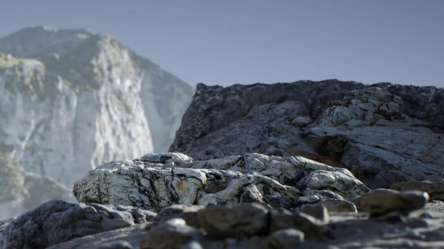 Rocks are seen in a mountainous location. The sun shines, creating shadows. The scene shows the natural landscape with cliffs in the background.
