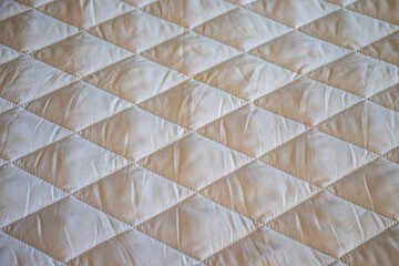 Fototapeta premium Beige quilted fabric texture with a geometric diamond pattern. Ideal backdrop for bedding catalogs, home textile website banners, or mattress manufacturing blogs.