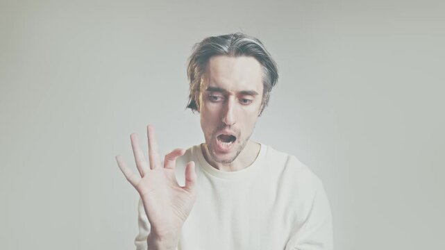 Young adult man making OK hand gesture, close-up portrait in white sweater against light gray background, multiple facial expressions, communication concept