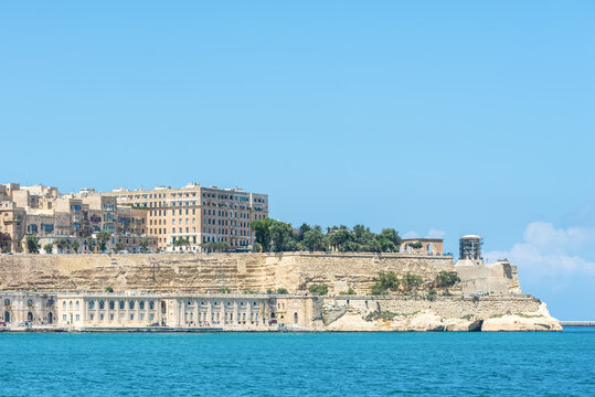 Panoramic view of Valletta waterfront and historic limestone bastions overlooking Grand Harbour in Malta. Mediterranean coastal architecture, blue sea and clear sky on a sunny day