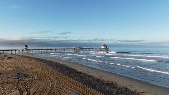 A low altitude aerial glide toward the Iconic Huntington Beach Pier. The drone starts it's flight from the shore and gently glides out over the waves of the Pacific Ocean.