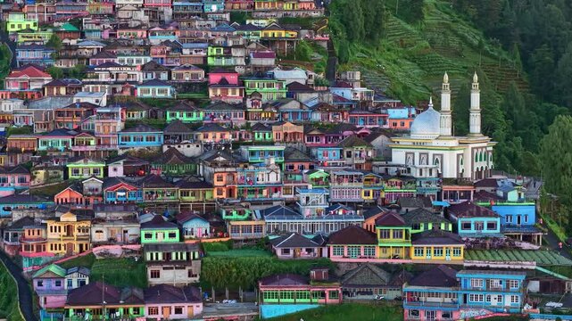 Aerial view of Rural hillside community surrounded by green mountains, colorful village buildings, and peaceful nature in cinematic daylight. Nepal Van Java, Indonesia.