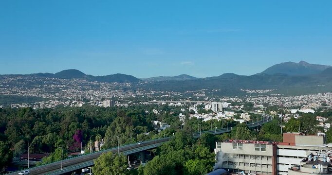 Full-color panoramic sunrise scene of urban infrastructure in southern Mexico City, with the Ajusco mountains rising in the background under warm morning light.