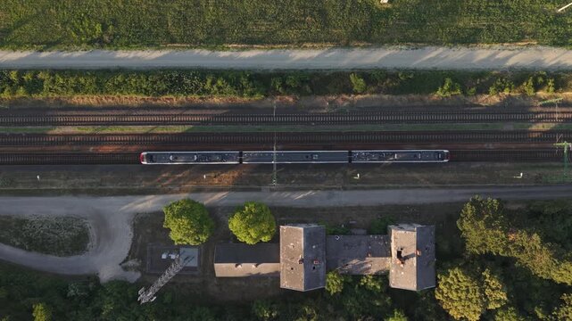 A top-down drone view of a modern passenger train traveling along parallel railway tracks through a rural landscape.