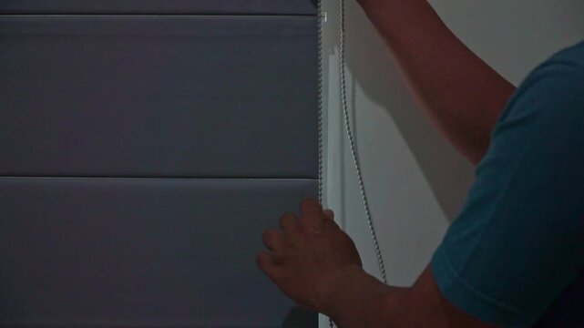 Person adjusting a roller curtain for better sunlight exposure. Residential interior scene emphasizing energy efficiency and natural lighting.