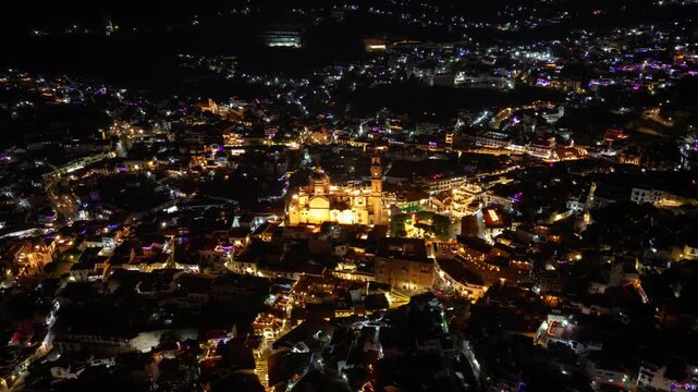 Aerial orbit hyperlapse establishing of Taxco, Mexico, with the Santa Prisca Parish at night, a trail of lights