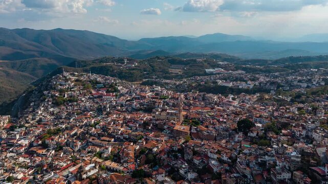 Aerial hyperlapse dolly in of Taxco, Mexico, colonial architecture with orange-tiled roofs and mountains in the background