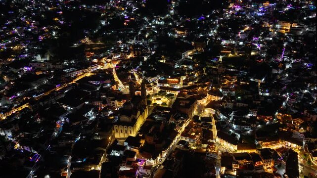 Aerial hyperlapse of Taxco, Mexico, at night, with a trail of lights from heavy traffic; a tourist destination featuring colonial architecture